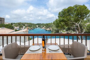 A balcony with a table set for two, overlooking a coastal area with a view of the sea and greenery. - Apartment 'Cala Figuera 2b' with Sea View, Wi-Fi and Air Conditioning (Cala Figuera)
