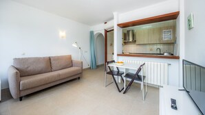 Una sala de estar con sofá, una mesa de comedor con sillas, televisor y una cocina con armarios y ventana.