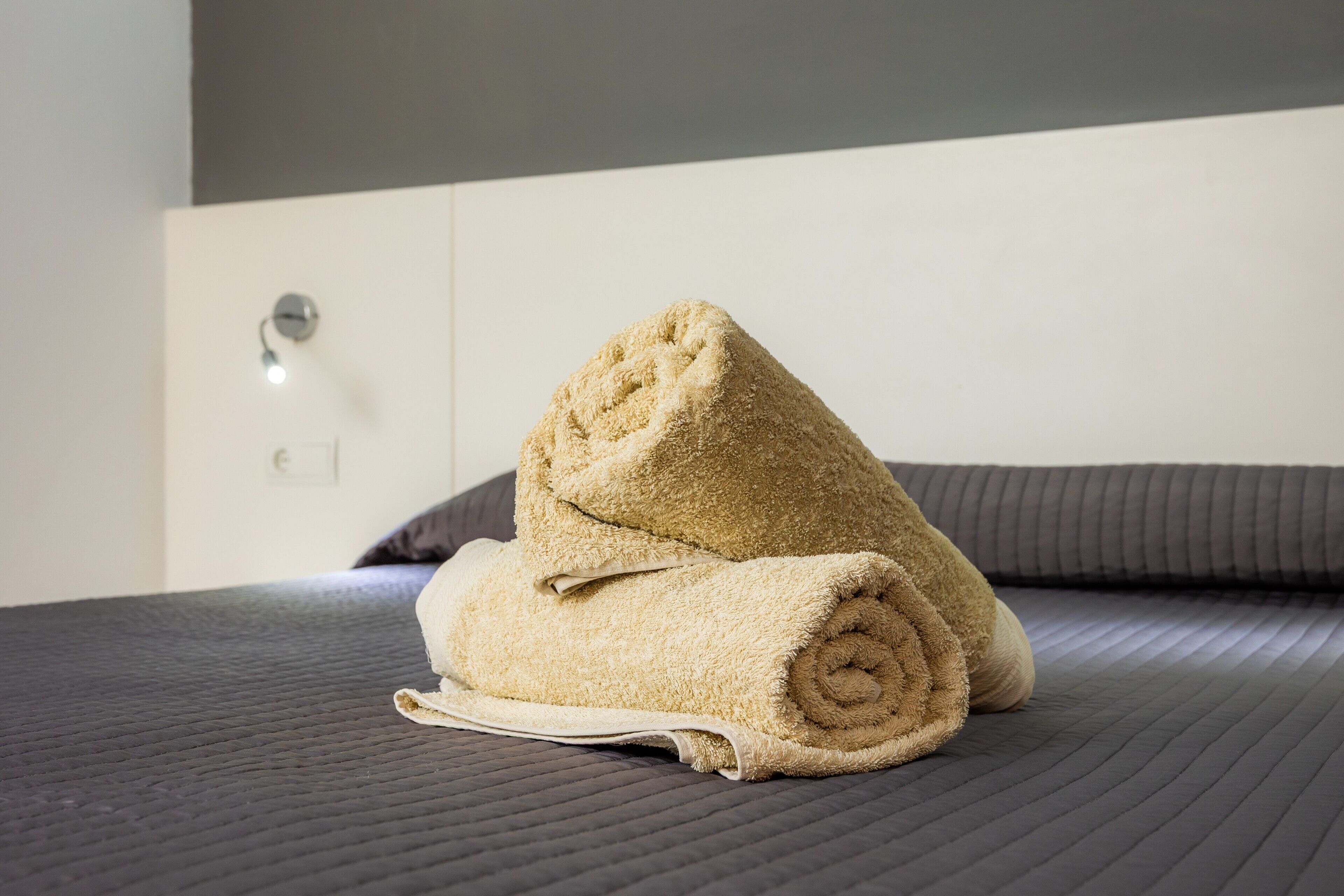 Ein ordentlich bezogenes Bett mit einem zusammengerollten Handtuch und einem Kopfkissen.