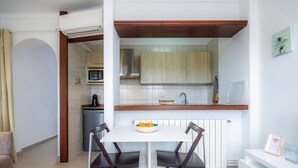 Une cuisine compacte avec des meubles blancs, un plan de travail blanc et un coin repas comprenant une table blanche et quatre chaises.