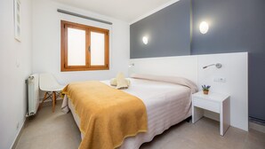 Une chambre à coucher comprenant un lit, une table de chevet, une chaise, un radiateur, une fenêtre et un luminaire fixé au mur.