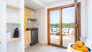 Una cocina equipada con horno integrado, cafetera y refrigerador. Cuenta con un comedor con mesa y sillas, y un balcón con vistas.