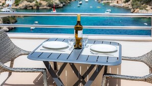 Une table avec une bouteille de vin, deux verres et des assiettes dressées pour deux personnes, donnant sur une zone côtière avec des bateaux et des bâtiments.