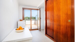Une pièce avec une table blanche, un saladier rempli d’oranges, une porte en bois et une porte-fenêtre coulissante donnant sur un espace extérieur.