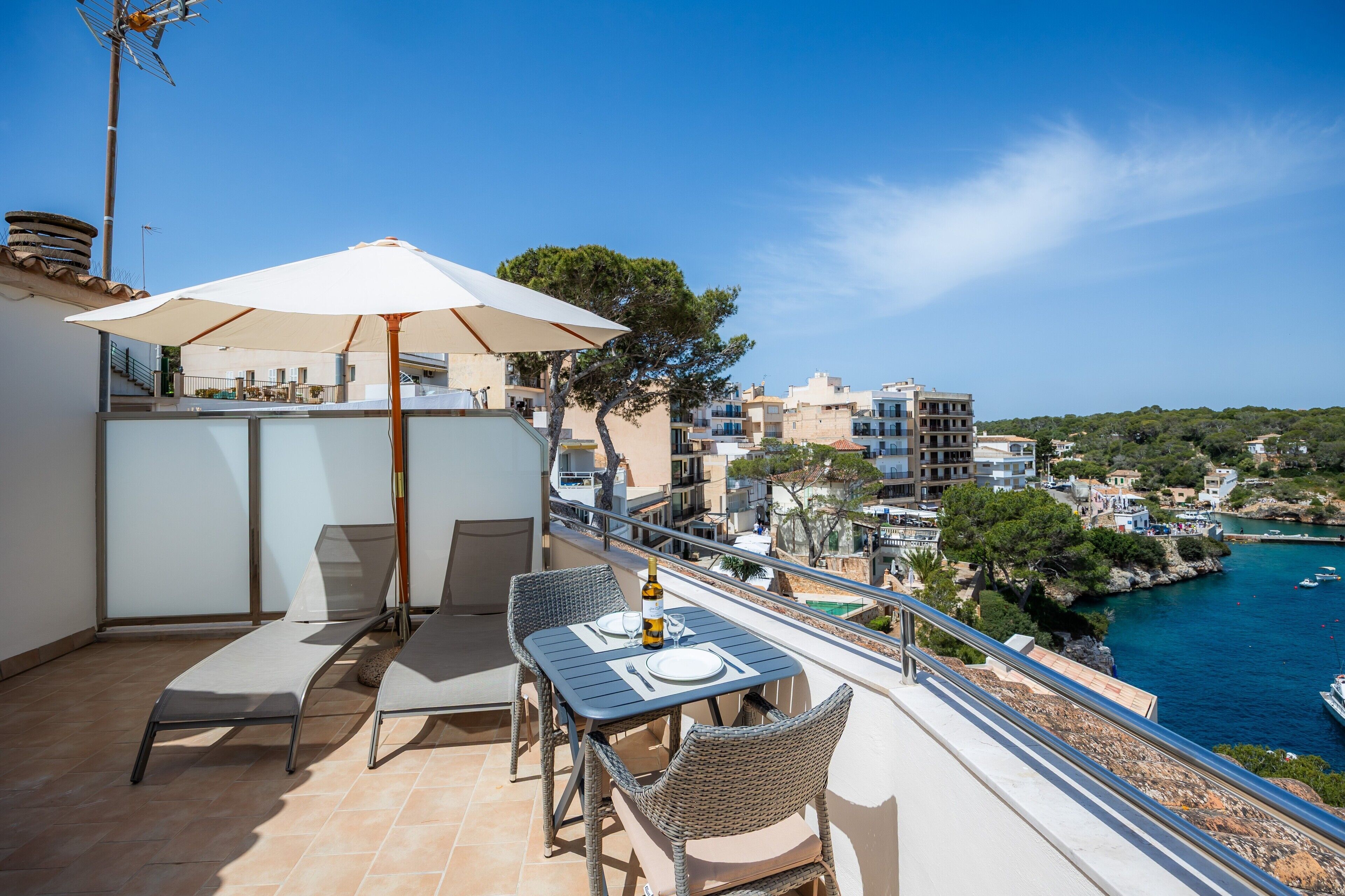 Ein Balkon mit Tisch, Stühlen und Sonnenschirm mit Blick auf eine Küstenstadt.