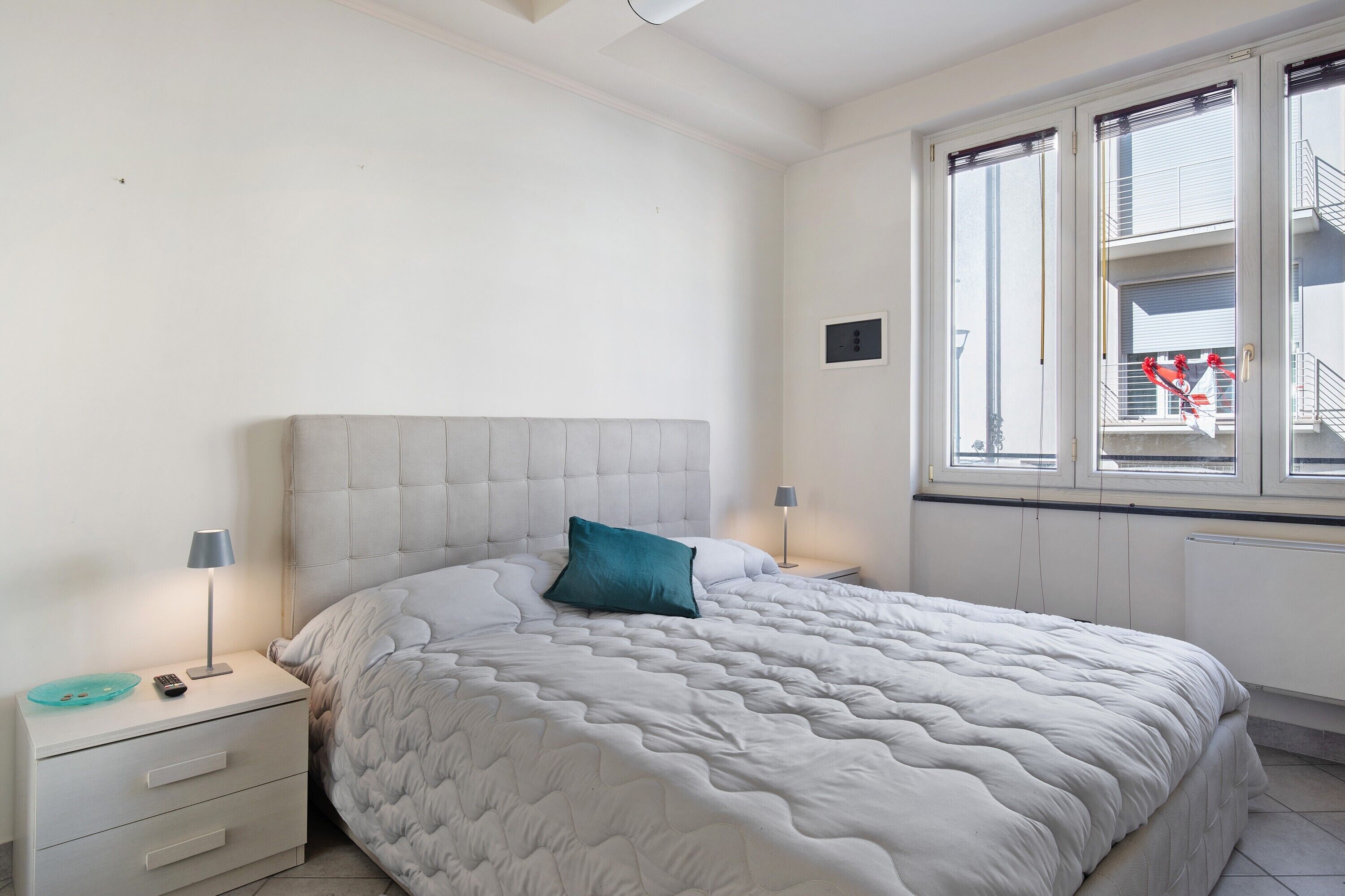 A bedroom with a bed, nightstand, lamp, and window with blinds.