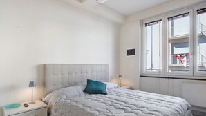 Et soveværelse med seng, sengebord, lampe og vindue med rullegardiner.