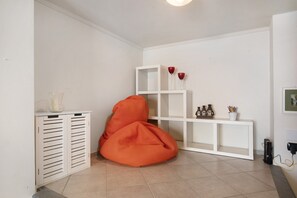 A room with a white cabinet, a white console table, a red bean bag chair, and a white shelving unit with decorative items.