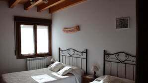 A bedroom with two beds, a window with curtains, a radiator, and a wooden sign on the wall.