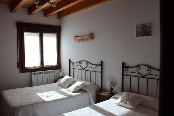 Un dormitorio con dos camas, una ventana con cortinas, un radiador y un cartel de madera en la pared.