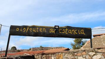 Una pared de piedra rústica con un letrero de madera que muestra el texto 'Disfruten su estadancia' en amarillo.