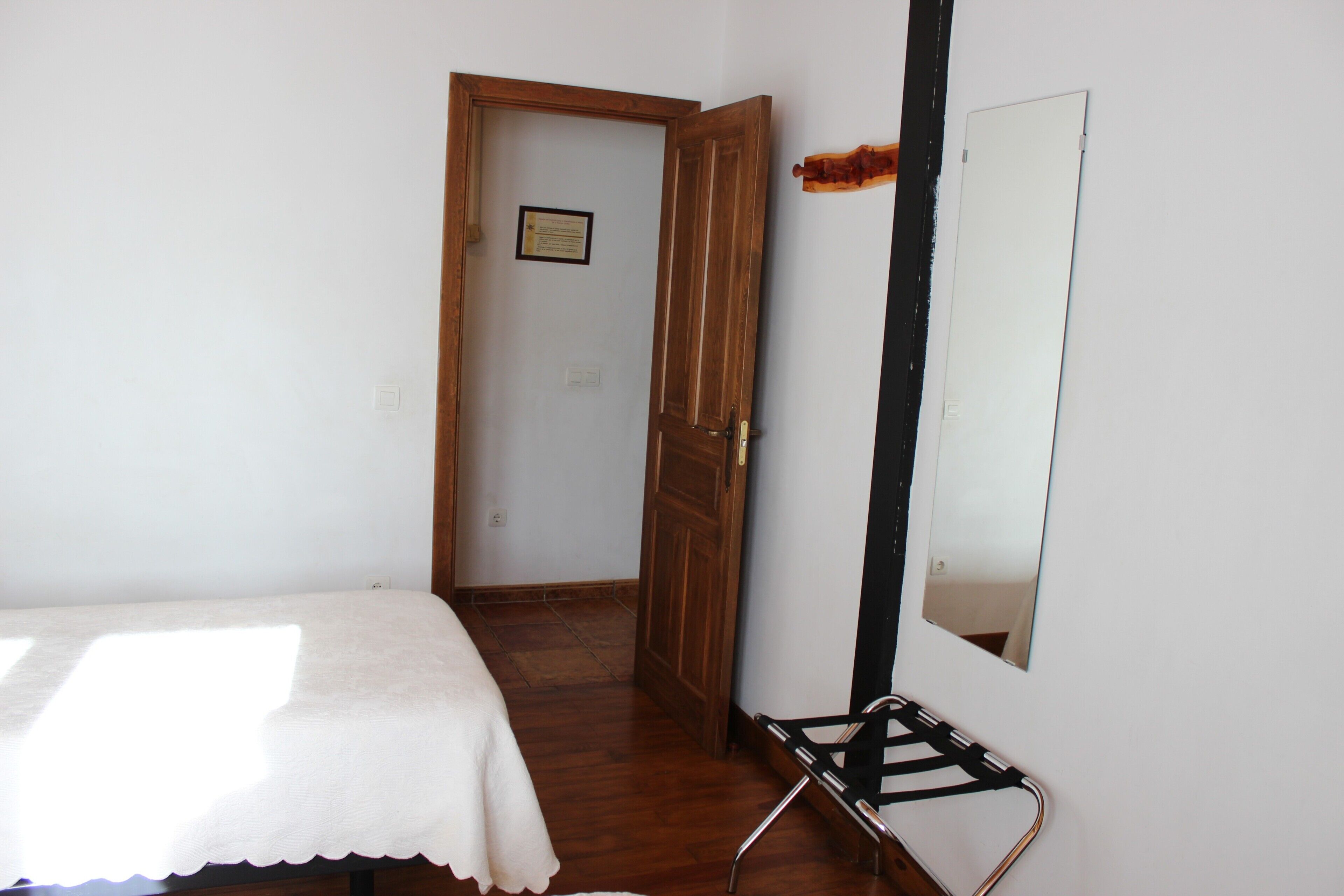Een kamer met een bed, een houten deur, een spiegel en een wandrek.