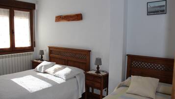 Een slaapkamer met twee bedden, houten hoofdeinden, een nachtkastje met een lamp, een aan de muur hangend kunstwerk en een raam met gordijnen.