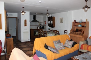 Ein Wohnzimmer mit einer Couch, einem Esstisch, Stühlen und einer Küchenzeile im Hintergrund.