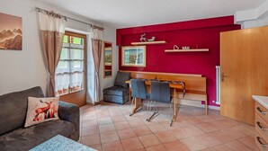 A room with a sofa, a dining table with chairs, a wooden cabinet, and a red accent wall.
