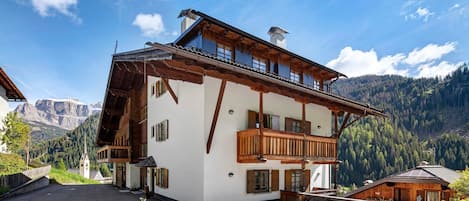 A two-story building with a balcony, a small attached structure, and a mountain backdrop.