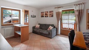 A room with a sofa, a small table, a radiator, a window with curtains, and wall art.