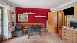 A compact living space with a dining table, two chairs, a sofa, a television, and a red accent wall.