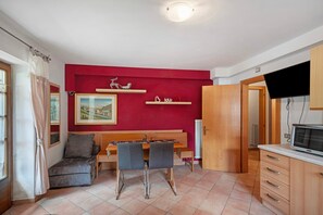 A compact living space with a dining table, two chairs, a sofa, a television, and a red accent wall. - Apartment 'App Camilla - Piano Terra' with Mountain View and Balcony (Canazei)