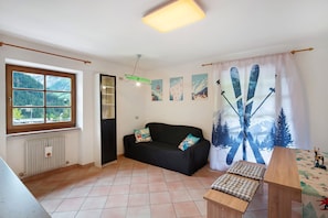 A room with a black sofa, a wooden table, a window with a view of mountains, and a ski-themed curtain.