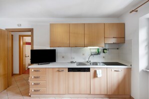Una cucina con mobili in legno, lavastoviglie e televisore.