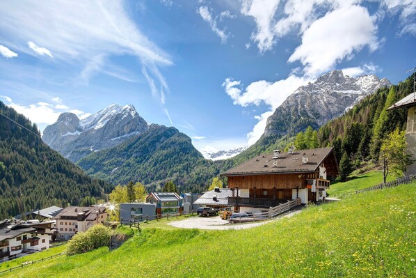 A mountain village with a wooden chalet, modern buildings, and a clear view of snow-capped peaks.