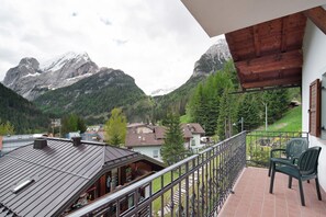 A balcony with a view of mountains, a chair, and a building with a metal roof.