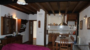 Una habitación con cama, muebles de madera, una zona de cocina con mesa y sillas, y un área pequeña cercada con un portón.