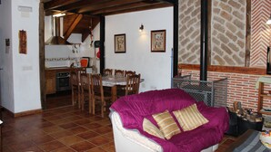 Comedor con mesa y sillas de madera, cocina al fondo y un sofá púrpura en primer plano.