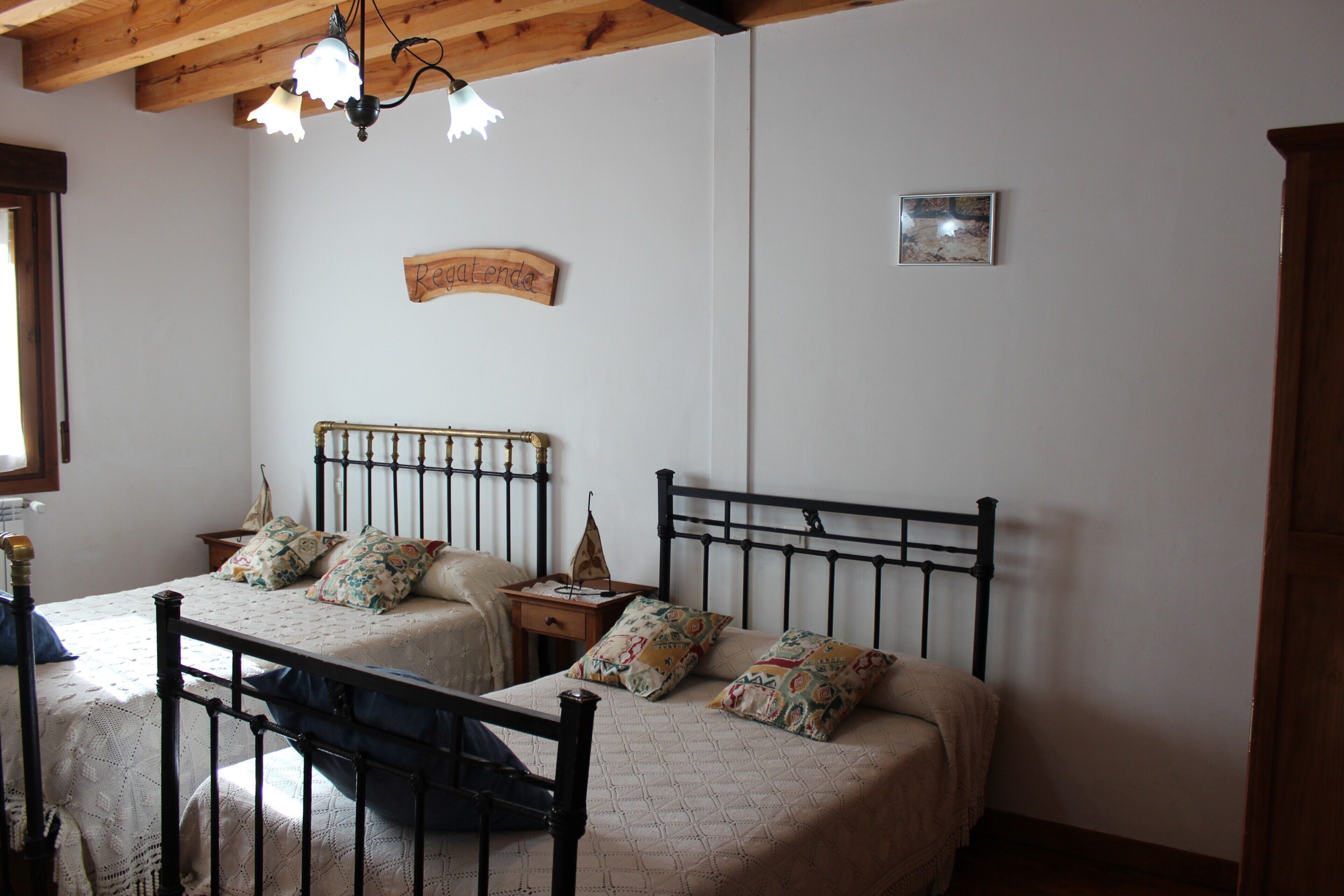 A bedroom with two beds, a wooden ceiling, a small table, and a wall-mounted sign.
