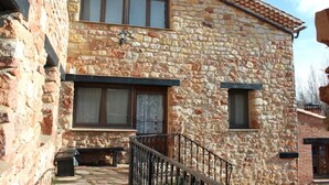 A stone building with two windows, a door, and a small porch with a bench.