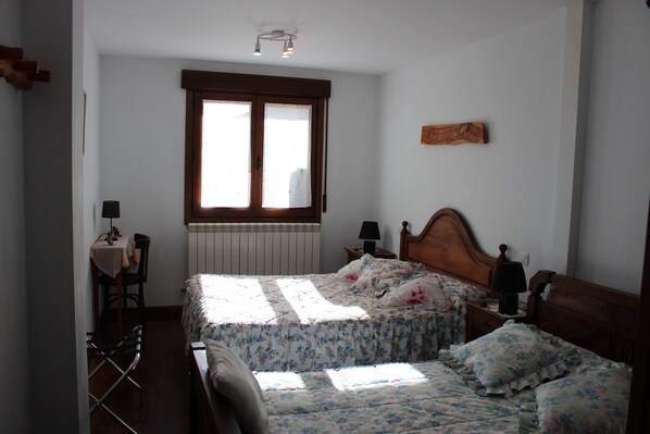 Un dormitorio con cama, ventana, radiador, una mesa con lámpara y una silla.