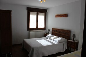 A bedroom with a bed, a window with curtains, a wooden headboard, a bedside table with a lamp, and a wall-mounted sign.