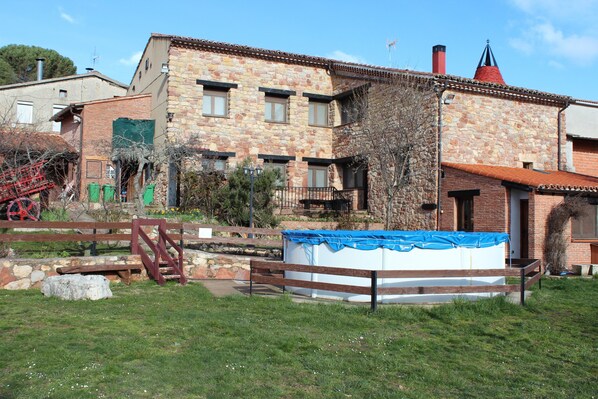 A stone building with a wooden deck, a covered swimming pool, and a red-roofed chimney.