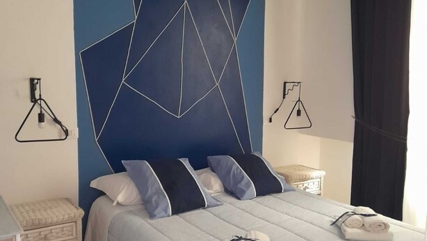 Une chambre à coucher avec un lit, des oreillers, une table de chevet, une lampe et un mur orné de motifs géométriques.
