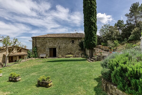 A stone building with a tiled roof, a grassy yard, and a tall tree.