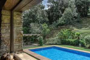 A stone wall, a swimming pool, and a patio area with a table and chairs.