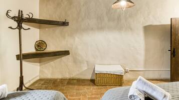 Una habitación con dos camas, un estante de madera, una cesta de mimbre, un perchero y una lámpara colgante.