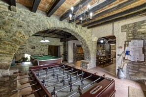 A room with a foosball table, stone walls, and a billiards table.
