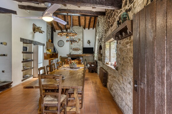 A rustic dining area with a wooden table and chairs, stone walls, and a ceiling fan.