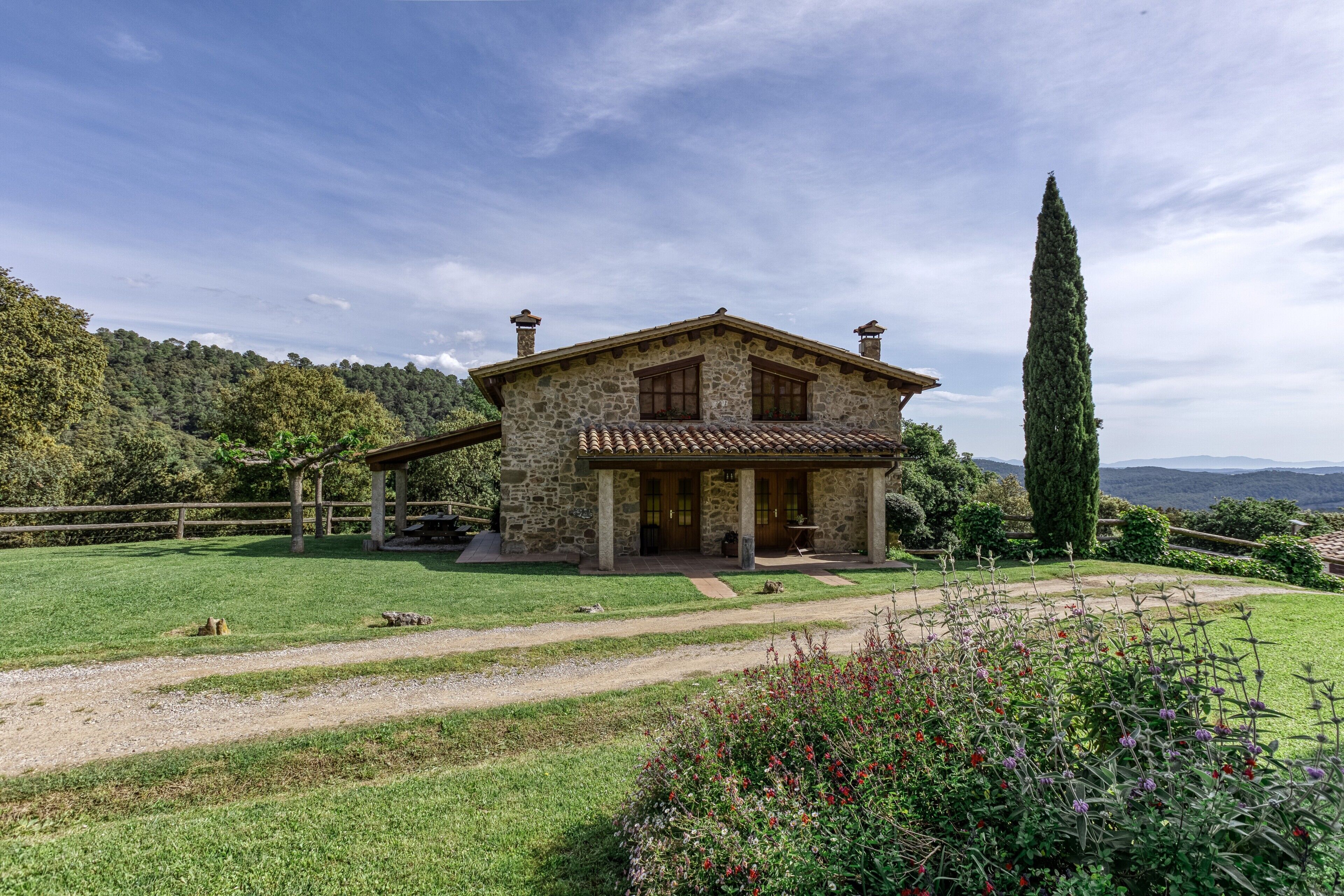 Una casa de piedra con un porche de madera, rodeada de un césped cuidado y un árbol alto.