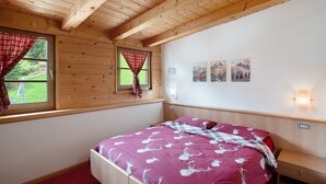 Ein Zimmer mit Holzwänden, einem Bett, einem Fenster mit Vorhängen und Wandbildern.