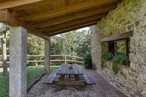 Ein Steinhaus mit einer Holzdiele, einem Picknicktisch und einer Steinsäule mit einem Fenster.