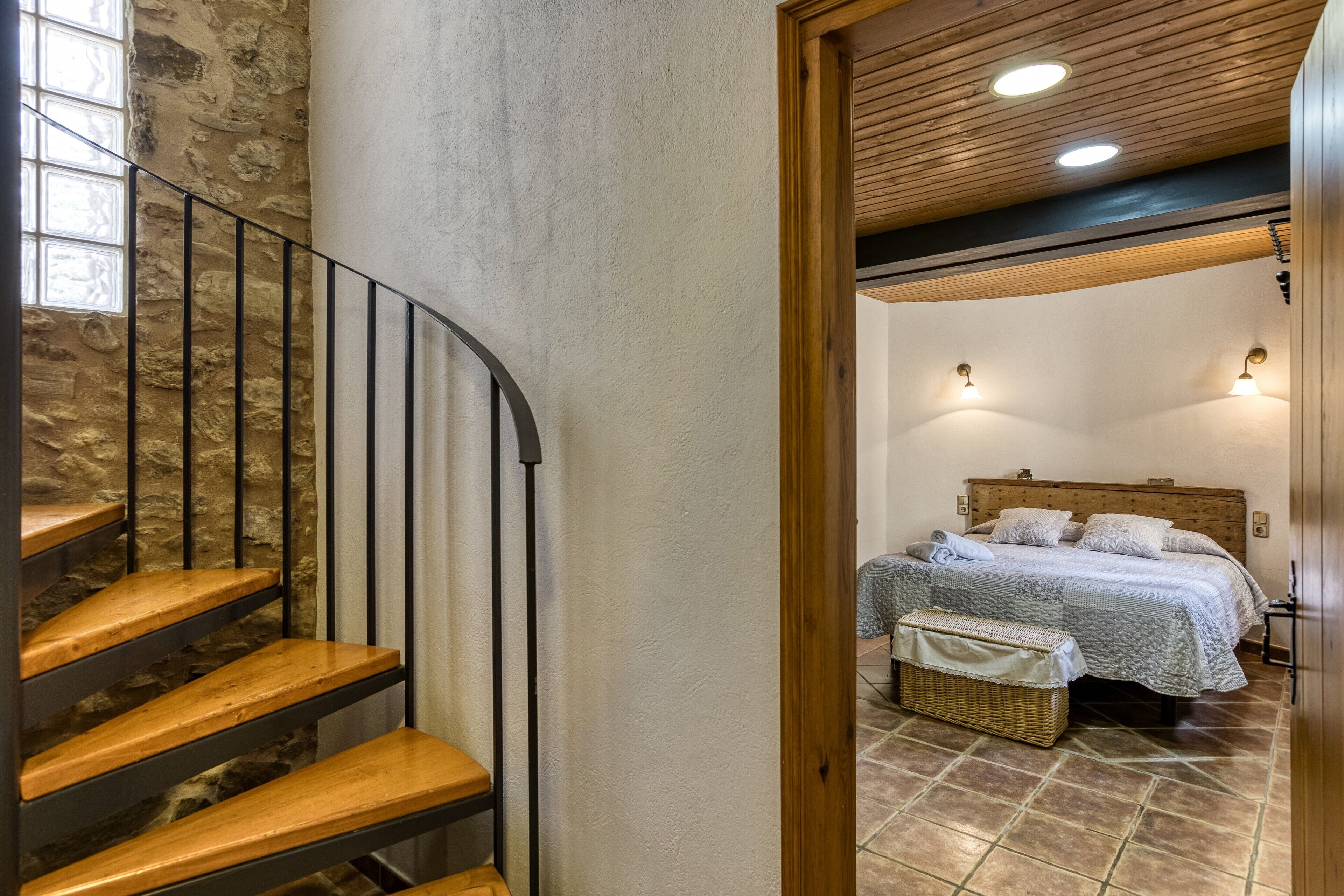 A staircase with wooden steps and metal railings, leading to a bedroom with a bed, pillows, and a bedside table.