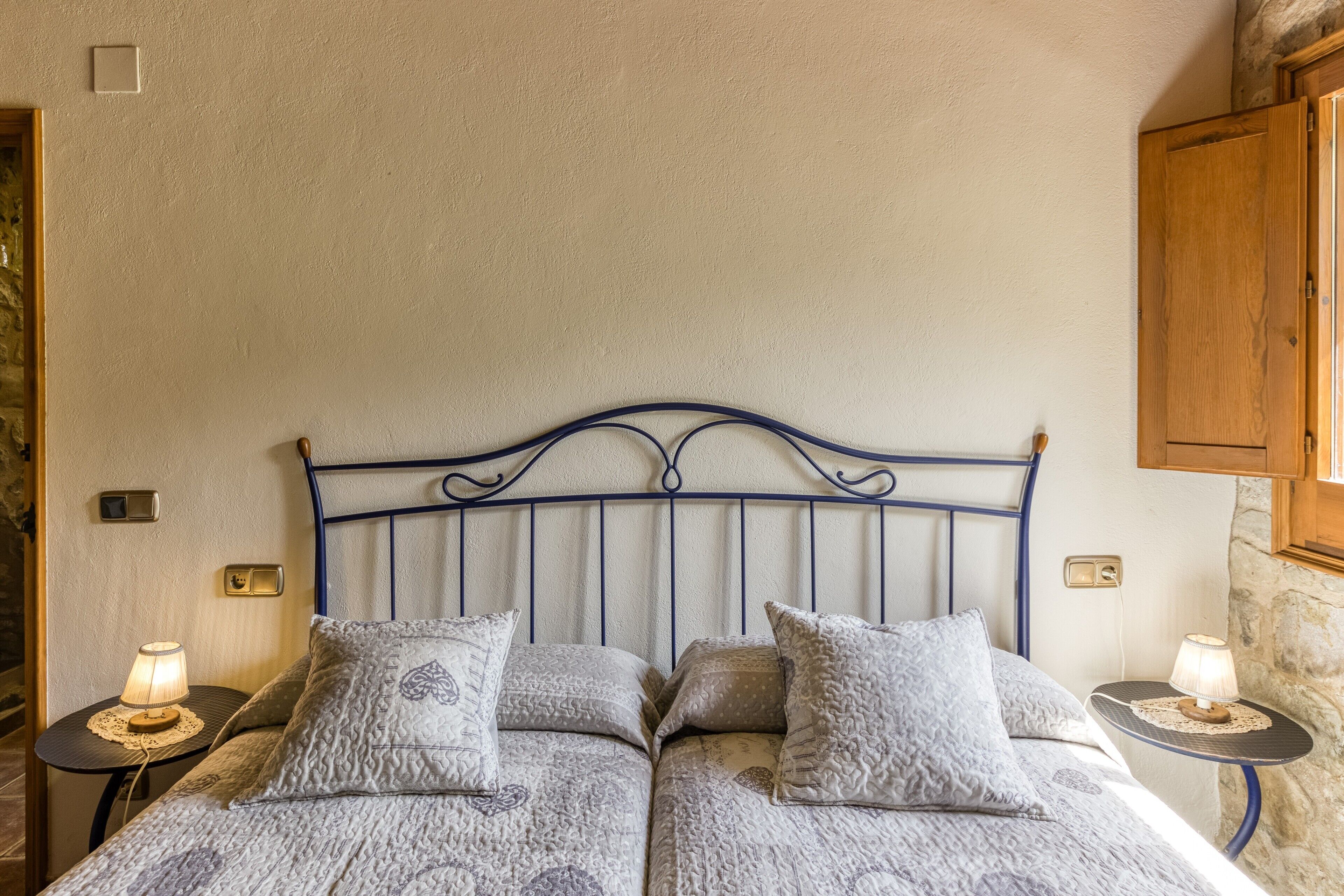Un lit double avec une tête de lit en métal, deux tables de chevet avec des lampes et un mur en pierre.