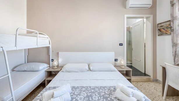 Een kamer met stapelbedden, een nachtkastje met lamp, een deur naar een andere kamer en een wandairconditioner.