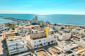 An aerial view of a coastal town with white buildings, a marina, and a clear blue sky.