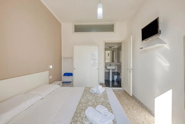 A hotel room with a bed, a TV mounted on the wall, a bathroom with a sink and mirror, and a small chair.