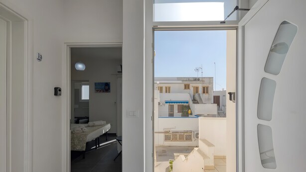 Ein modernes Apartment mit Balkon, einem Bett, einem Schreibtisch und Blick auf angrenzende Gebäude.