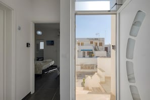 A modern apartment with a balcony, a bed, a desk, and a view of neighboring buildings.